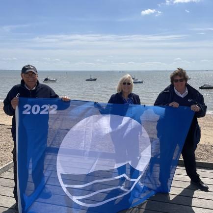 Councillor Mulroney and officers holding Blue Flag 2022 in front of a beach.