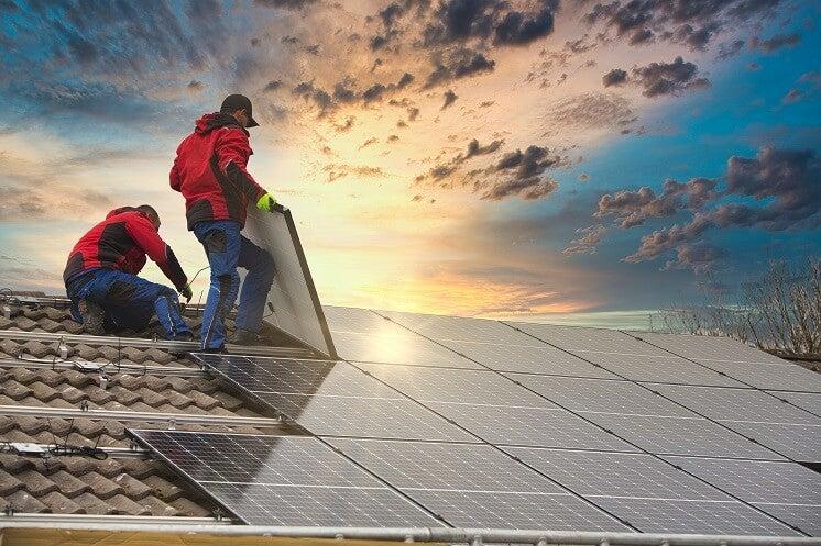 Two people installing solar panels on roof