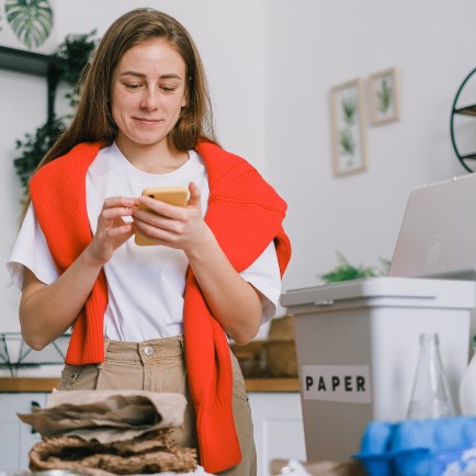 Lady in her kitchen recycling paper whilst looking at her mobile phone.